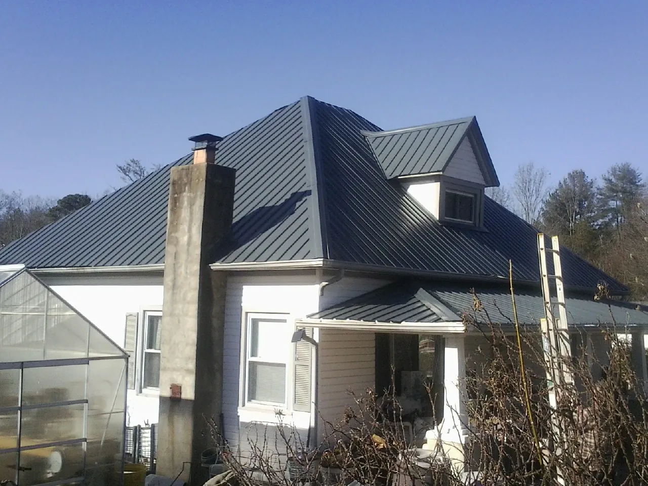 Dark blue standing seam metal roof on a white farmhouse with dormer — Slate & Tile Roof Repair by Roofing Brothers in Slaughters
