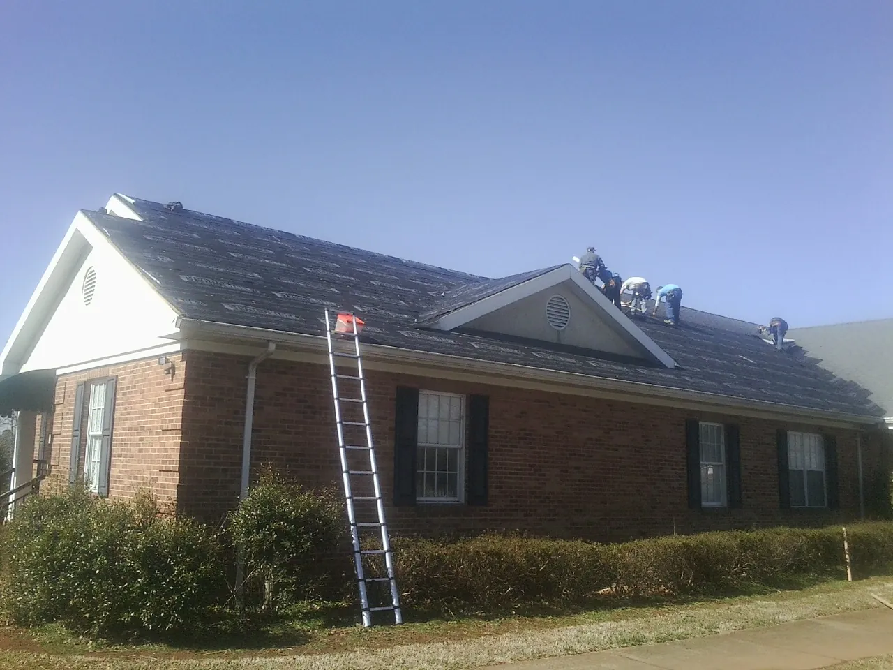 Crew tearing shingles off a brick ranch roof with a ladder set — Emergency Roof Repair work by our crew in Slaughters