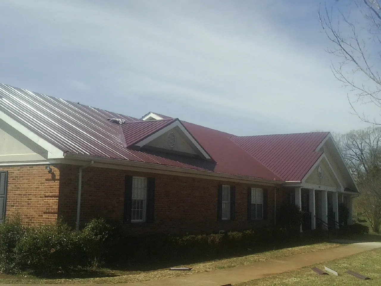 Red metal roof with gabled entries on a long brick building, from a Hail Damage Roof Repair job in Slaughters
