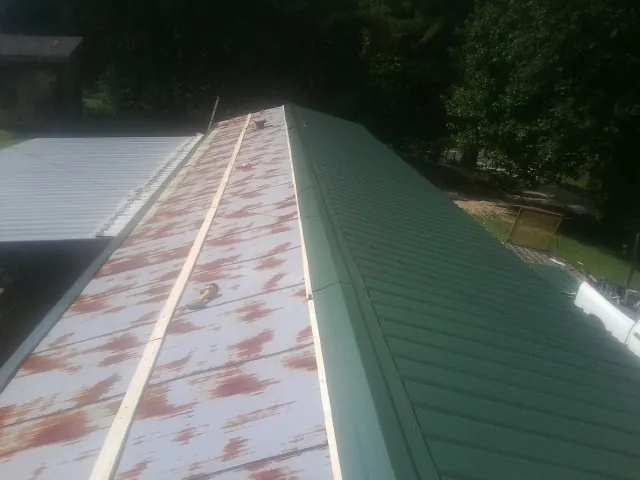 Old rusted panels beside newly installed green metal roofing — Wind Damage Roof Repair by Roofing Brothers in Slaughters