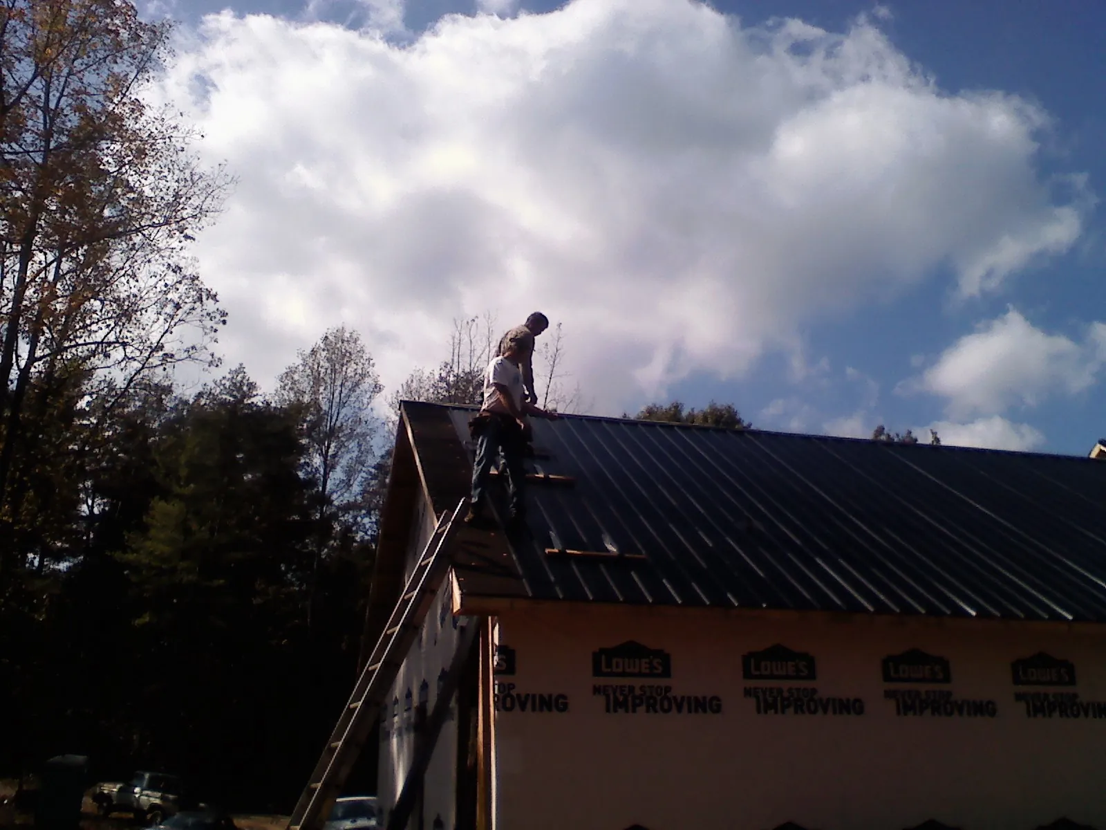 Roofer fastening dark metal panels high against a cloudy sky, from a Roof Inspection job in Slaughters