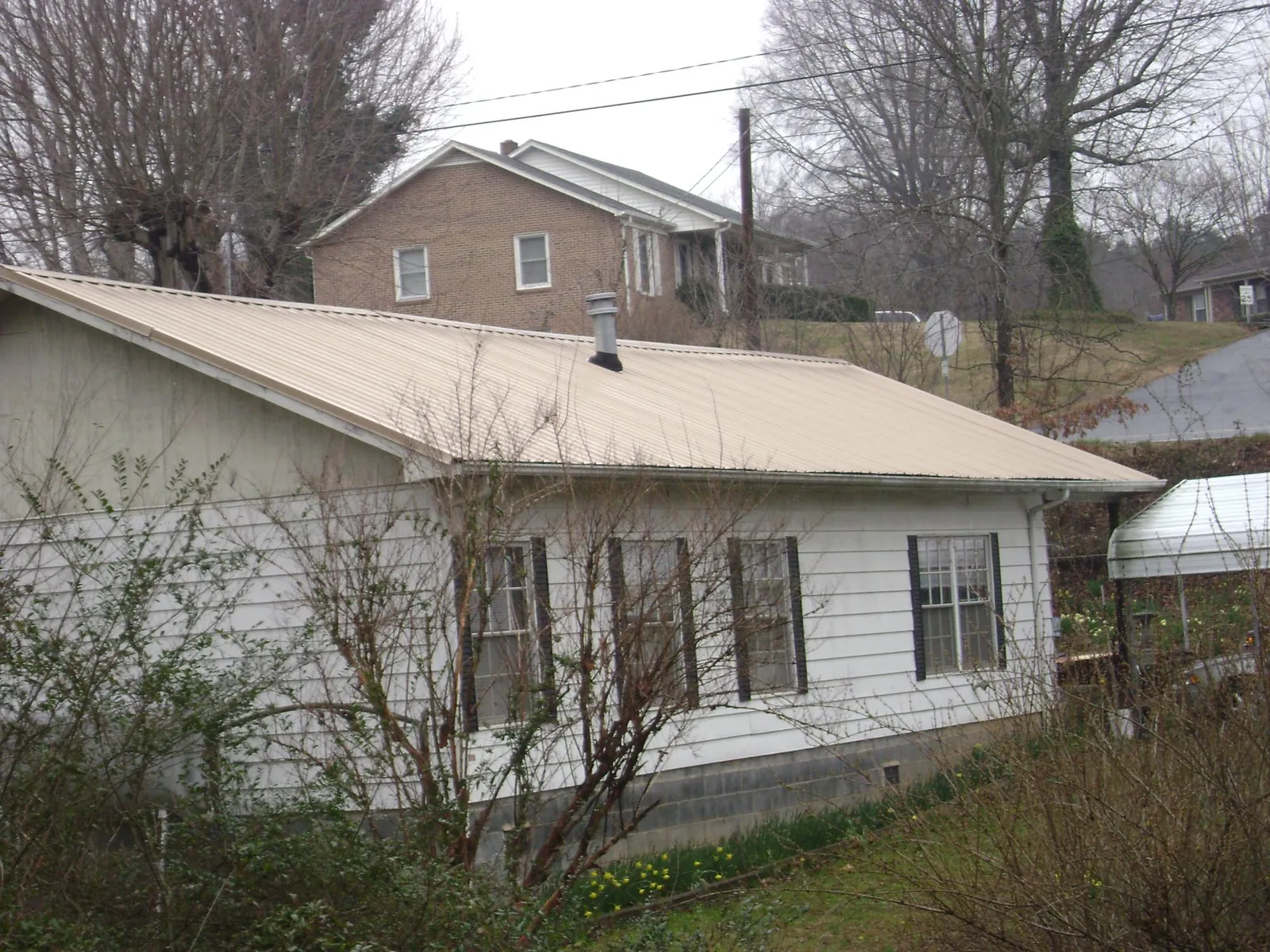 Tan metal roof on a white sided house set into a hillside — Commercial Roofing by Roofing Brothers in Slaughters